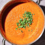 A pot of creamy tomato soup, enriched with Homemade-ish Marinara Sauce and topped with freshly chopped basil, sits on a gray surface.