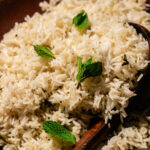 A close-up of a plate of cooked Mint Rice, garnished with fresh mint leaves, with a wooden serving spoon resting on the rice.