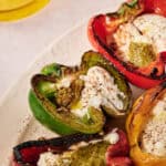 Charred peppers with Stracciatella and pesto: Grilled red, green, and yellow bell peppers stuffed with creamy Stracciatella cheese and vibrant green pesto sauce, served on a white plate with a sprinkle of seasoning.