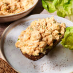 A slice of dark bread topped with creamy egg salad sits on a plate, creating a delicious open-faced Egg Salad Sandwich, with lettuce leaves nearby and a bowl of egg salad in the background.