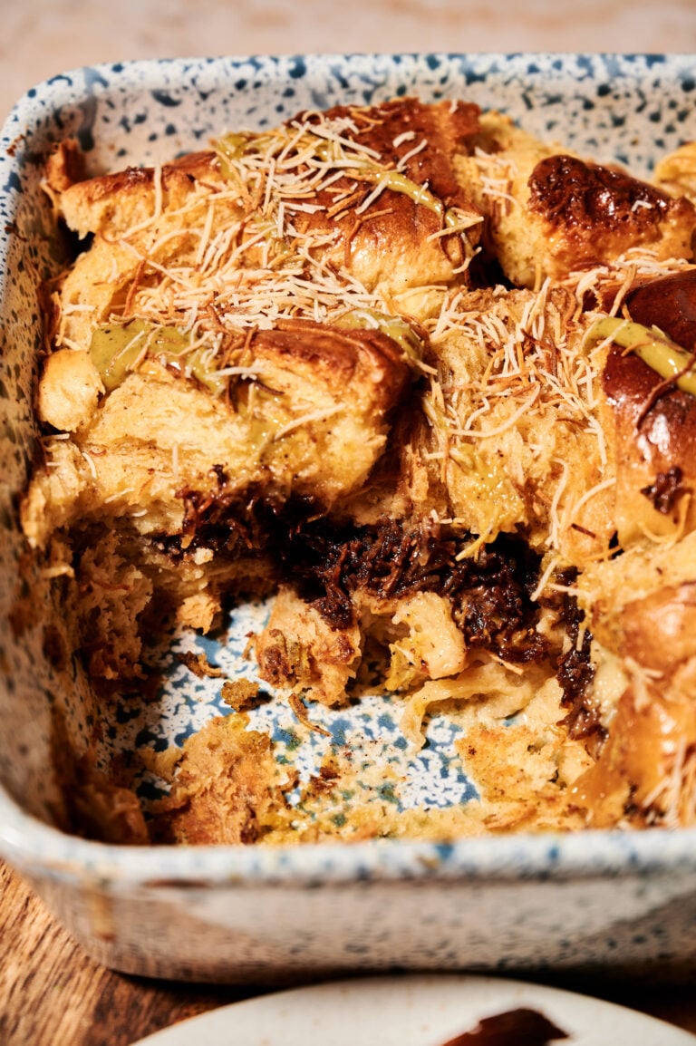 Blue and white casserole dish with layer Dubai chocolate French toast casserole you can see the bottom layer of the challah bread, the middle layer of the kataifi pastry with chocolate and pistachio cream and another top layer of the hollow bread. It looks fluffy and moist crispy on the edges.