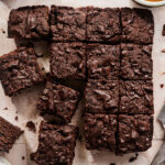 Overhead view of chocolate brownies cut into squares on parchment paper, with a bowl of orange puree and a knife nearby.