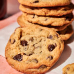 Stack of homemade chocolate chip cookies with golden edges and gooey chocolate chips, photographed on a pink surface for easy, classic chocolate chip cookie recipe.