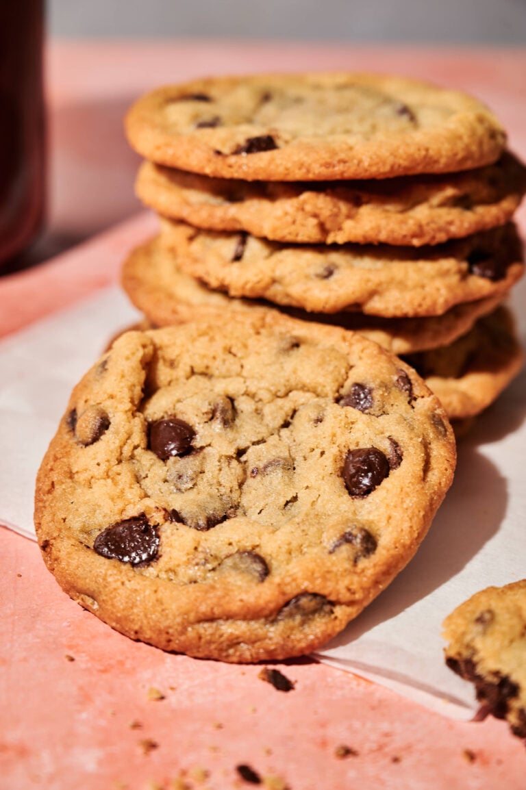 Stack of homemade chocolate chip cookies with golden edges and gooey chocolate chips, photographed on a pink surface for easy, classic chocolate chip cookie recipe.