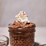 Jar of high-protein chocolate mousse made without protein powder, topped with whipped cream and cocoa dust, photographed slightly pulled back to show texture and presentation for Smith’s in Bloom.