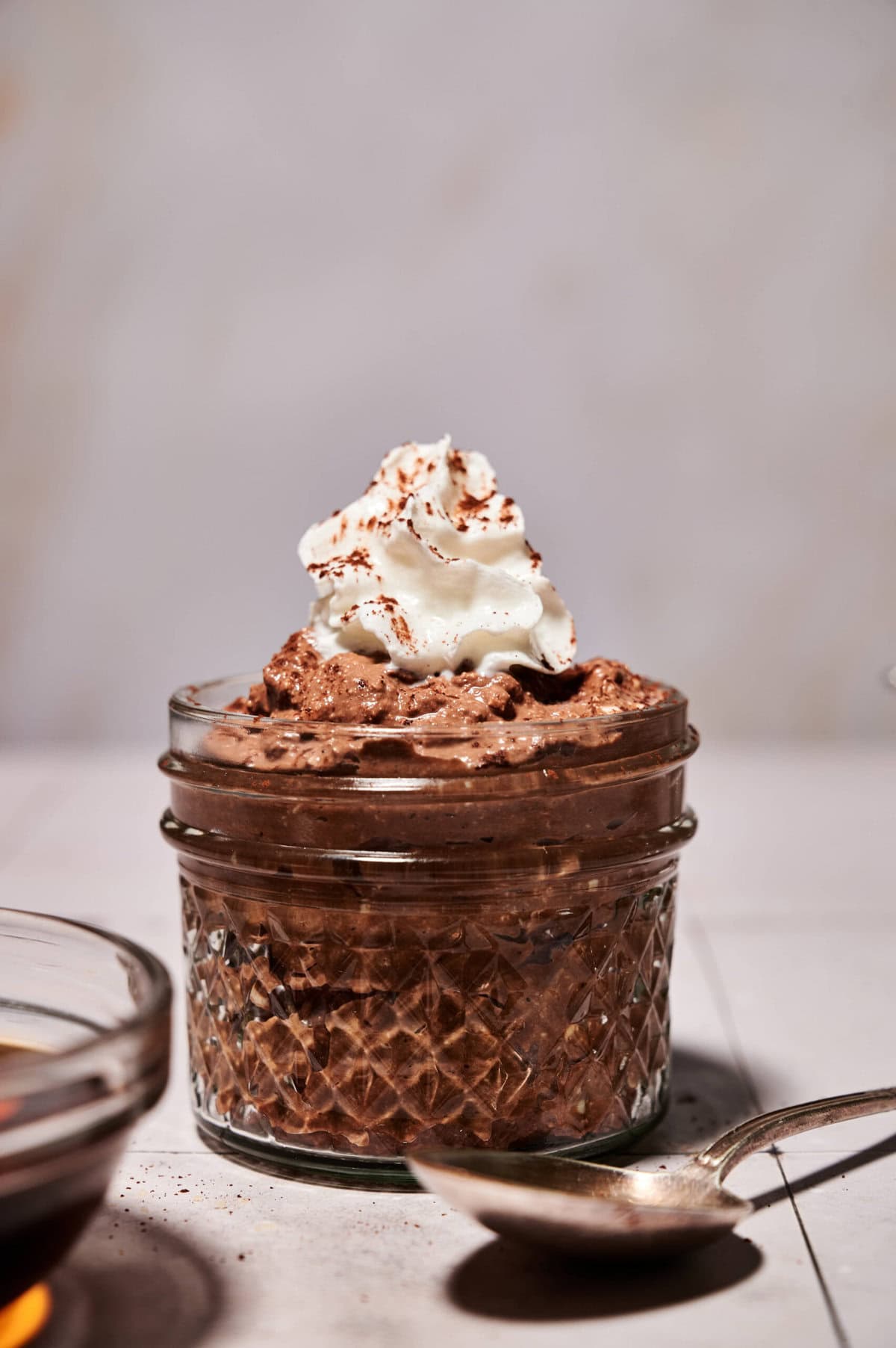 Jar of high-protein chocolate mousse made without protein powder, topped with whipped cream and cocoa dust, photographed slightly pulled back to show texture and presentation for Smith’s in Bloom.