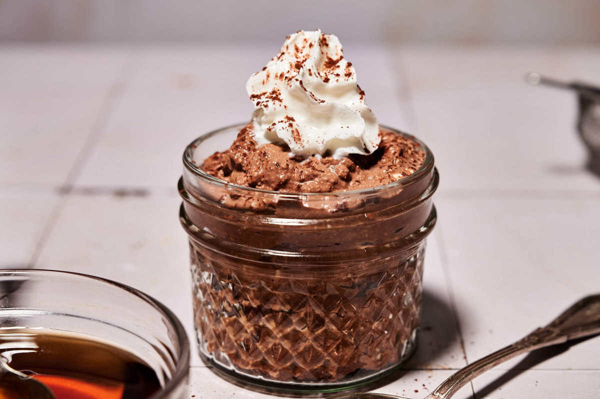 Horizontal wide shot of simple high-protein chocolate mousse without protein powder in a glass jar, topped with whipped cream and cocoa dust, styled on a light surface for Smith’s in Bloom.