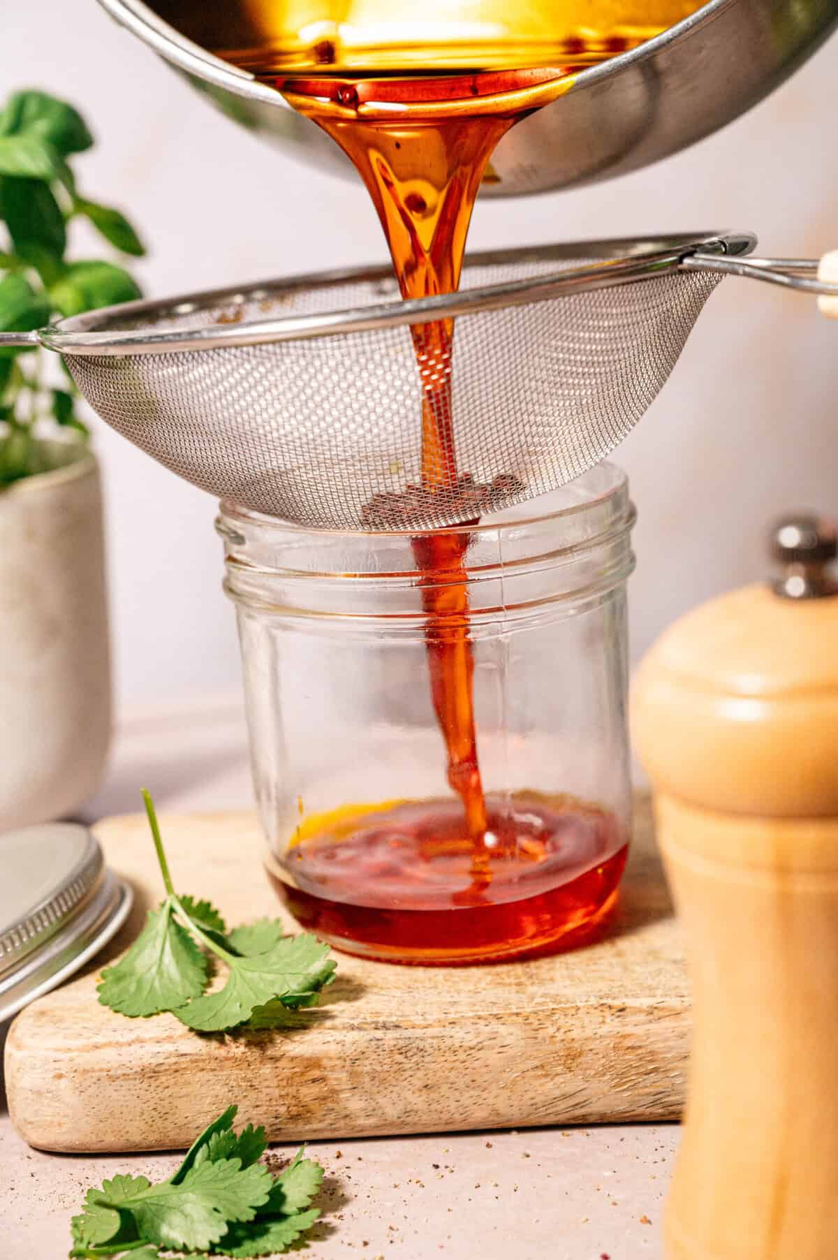 (oil being strained into jar): Straining homemade achiote oil through a fine mesh sieve into a glass jar, capturing its vibrant red/orange hue.