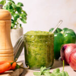 Open jar filled with bright green homemade sofrito with spoon inside, surrounded by bell pepper, red onion and herbs for an easy 5?minute flavor base.