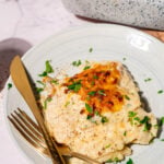 Creamy cheesy scalloped potatoes on a plate with golden brown crust, sprinkled with fresh parsley and served with gold fork and knife.