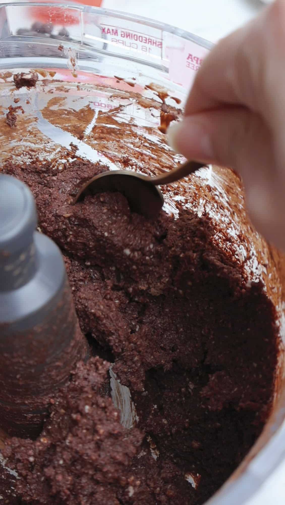 Thick cocoa date and cashew mixture being scooped from a food processor for chocolate truffles.
