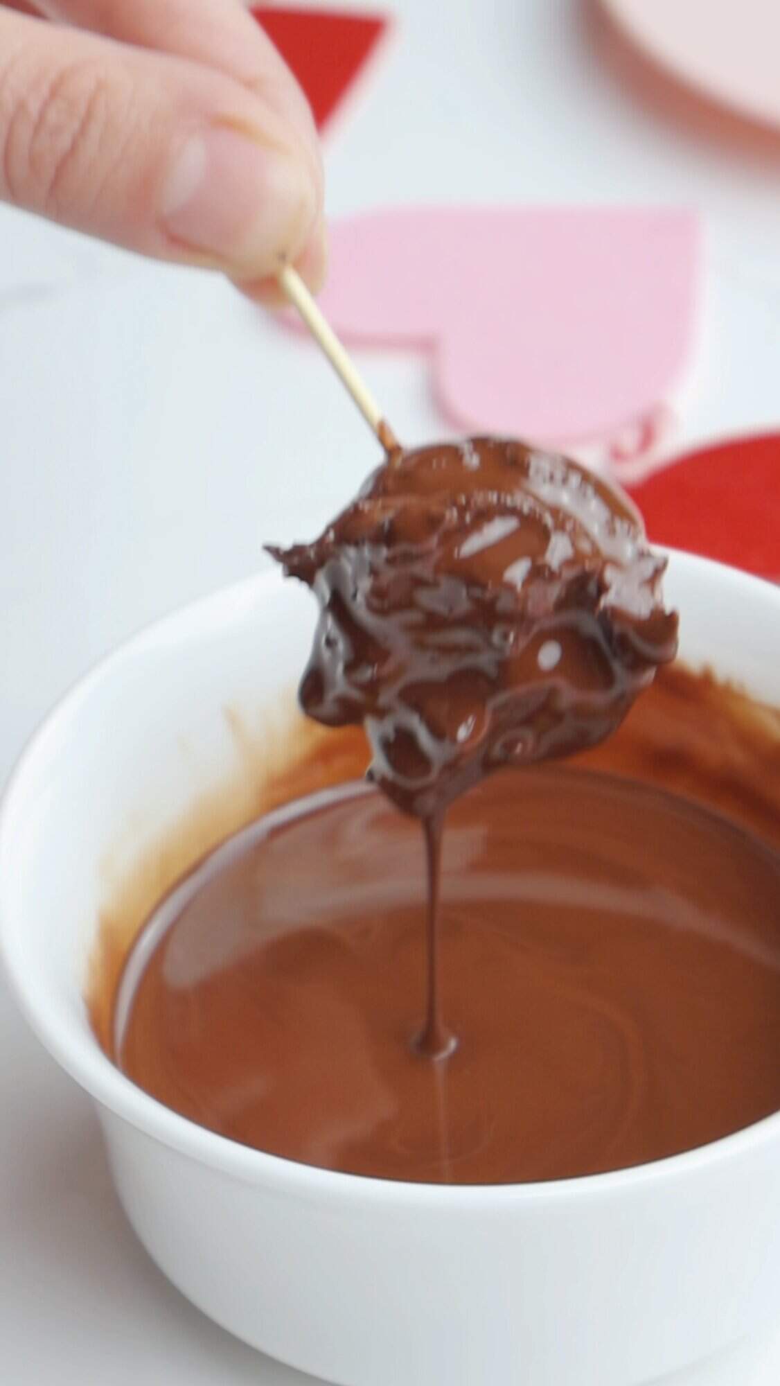 Hand dipping a raspberry cocoa truffle into a bowl of melted chocolate using a toothpick