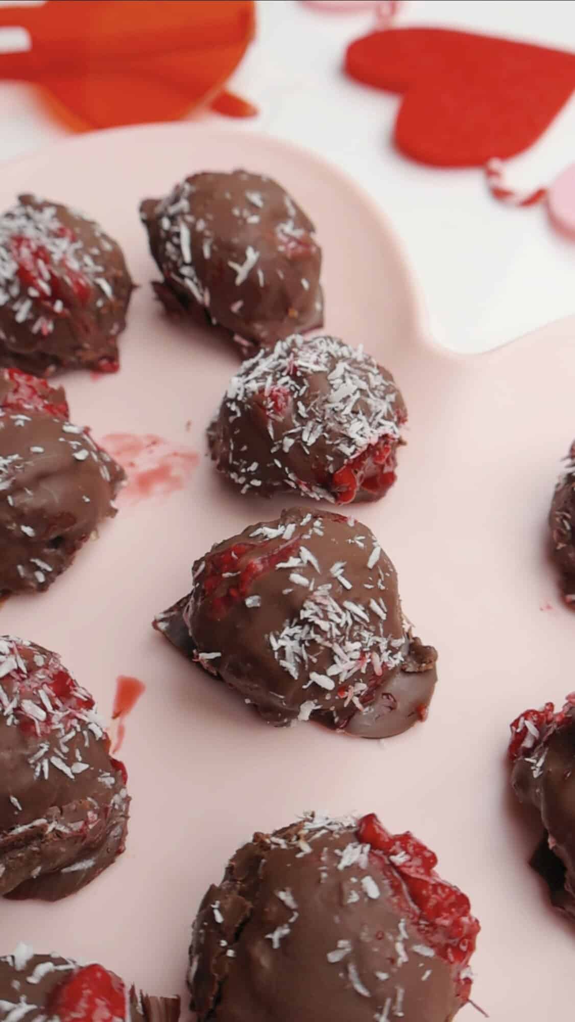 Close up of healthy raspberry chocolate truffles topped with shredded coconut, arranged on a pink heart-shaped tray for Valentine’s dessert