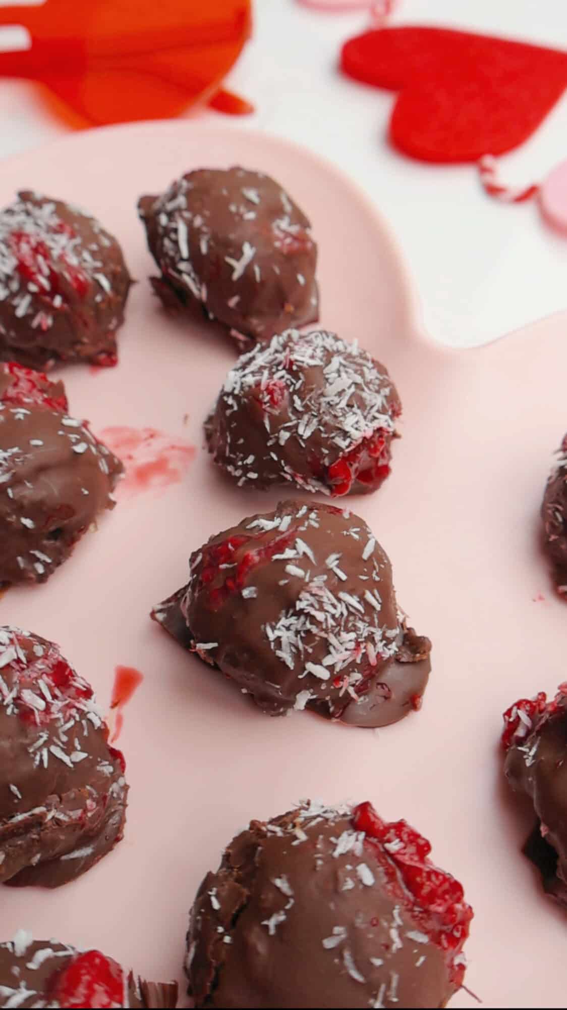 Close up of healthy raspberry chocolate truffles topped with shredded coconut, arranged on a pink heart-shaped tray for Valentine’s dessert