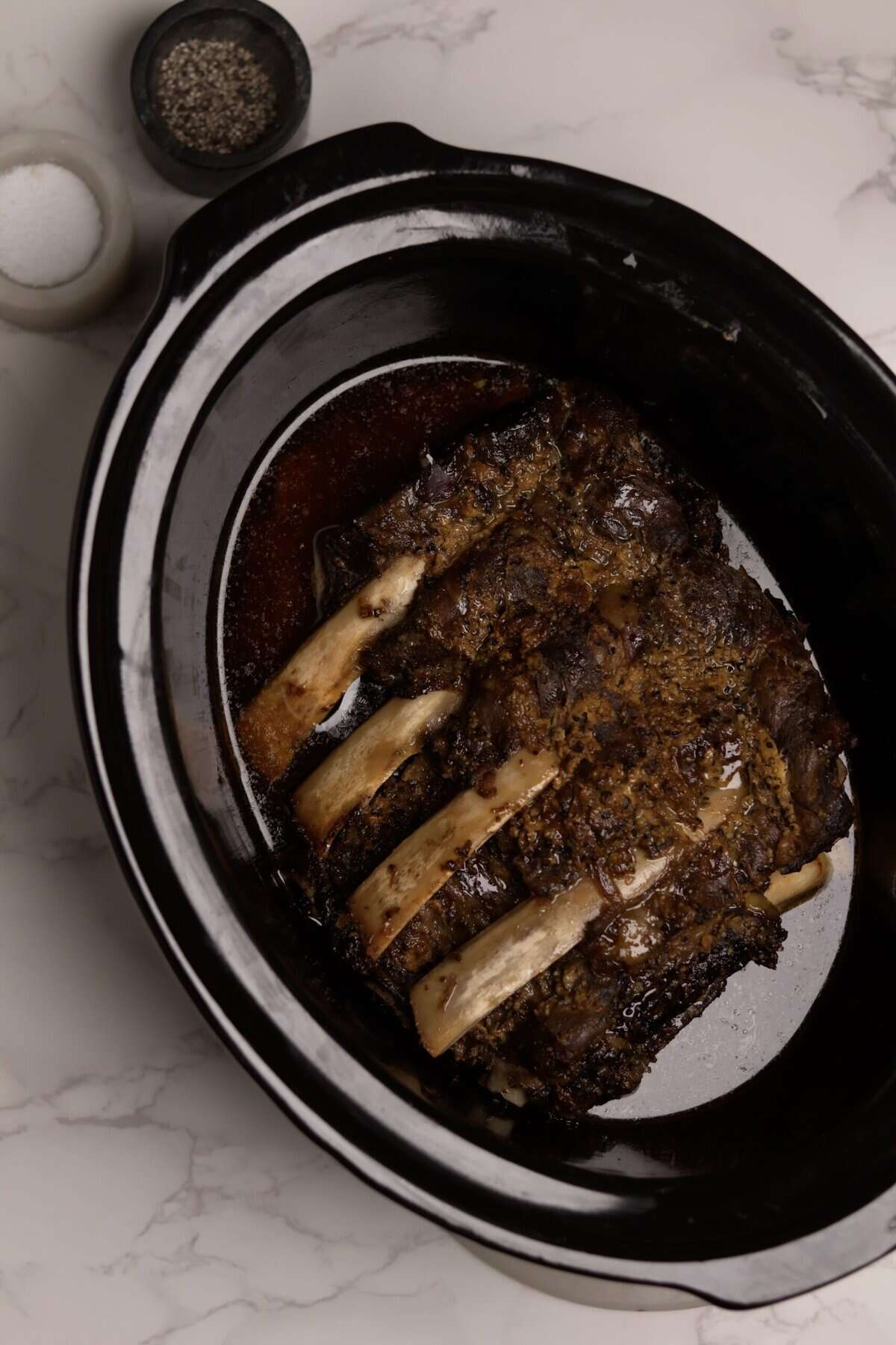 Overhead shot of crockpot baby back ribs fully cooked in the slow cooker, resting in their cooking juices and ready to be transferred to a baking sheet and brushed with BBQ sauce
