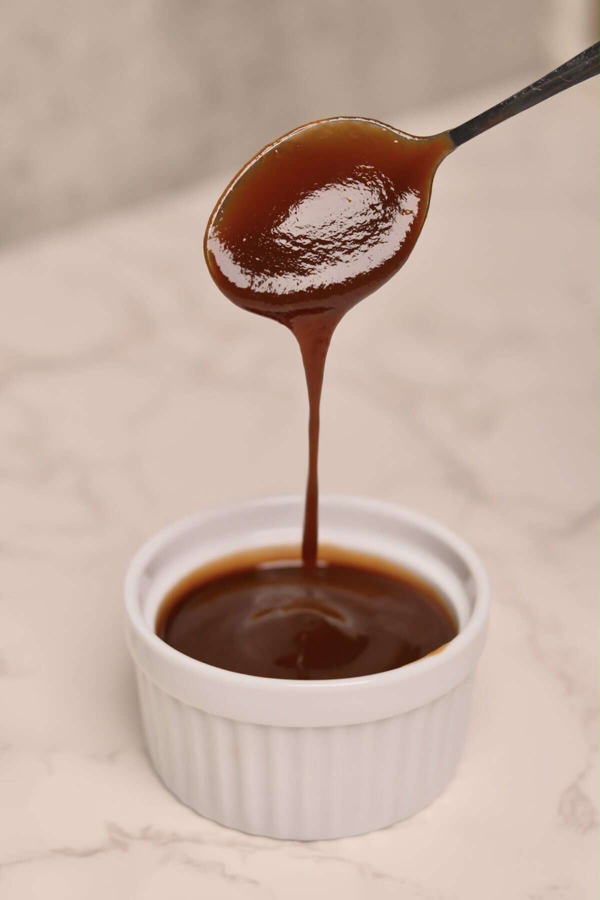 “Whisking thick homemade apple cider barbecue sauce in an enameled pot on the stovetop.