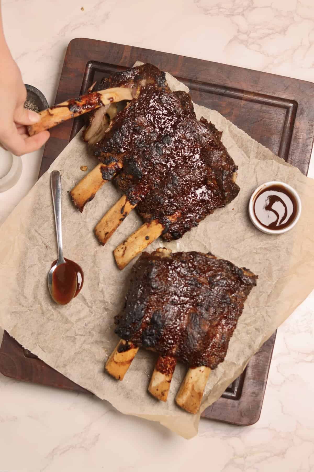 Overhead shot of crockpot baby back ribs on a sheet pan while a hand pours glossy BBQ sauce over the tender beef back ribs