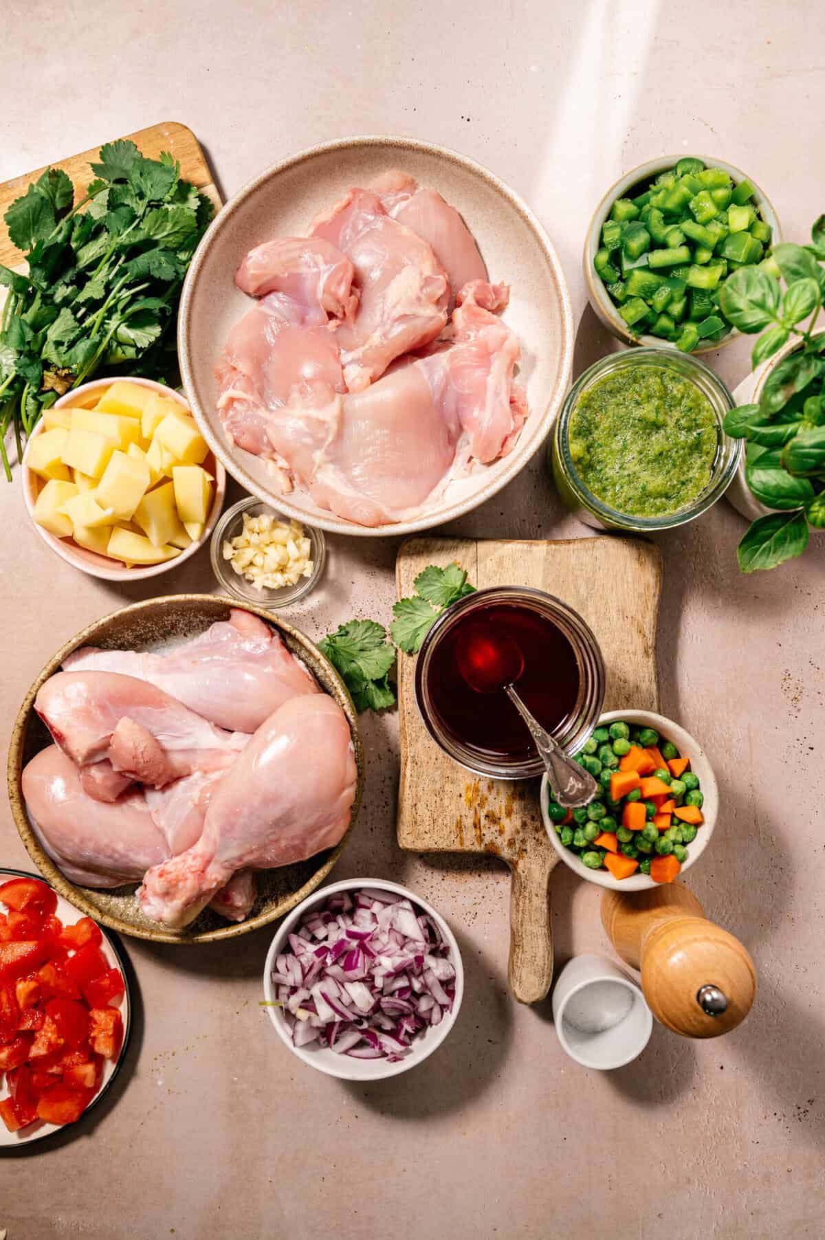 Ingredients for seco de pollo ecuatoriano including chicken, aliño, potatoes, onions, peppers, peas, carrots, tomato, cilantro, and achiote oil arranged on a counter.