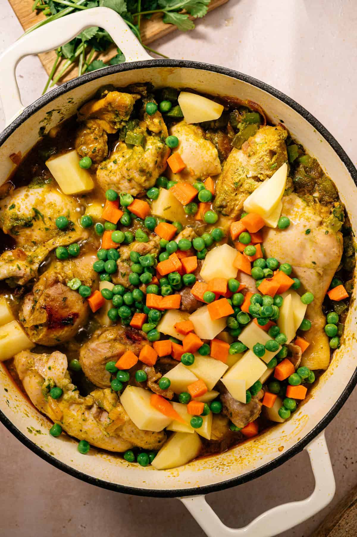 Dutch oven filled with simmering seco de pollo ecuatoriano topped with potatoes, peas, and carrots before finishing the stew.