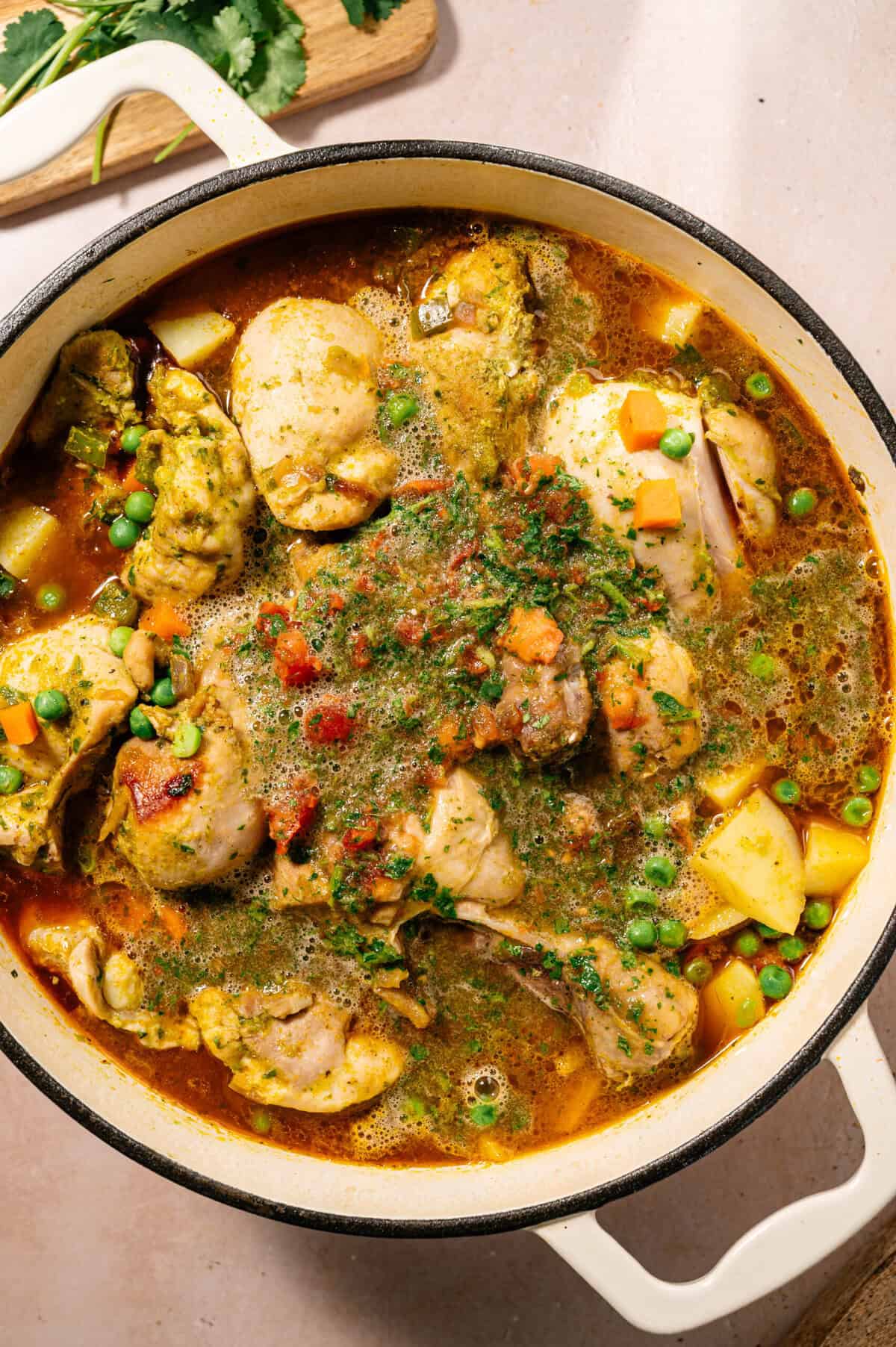 Pot of seco de pollo ecuatoriano simmering with chicken, potatoes, peas, carrots, and tomato cilantro sauce.