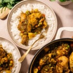 Bowls of seco de pollo ecuatoriano served over white rice with peas, carrots, and potatoes alongside fresh cilantro and green alino sauce