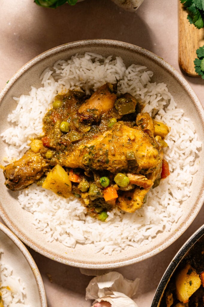 Close up of seco de pollo ecuatoriano chicken stew with potatoes, peas, and carrots served over white rice in a bowl with a gold fork.