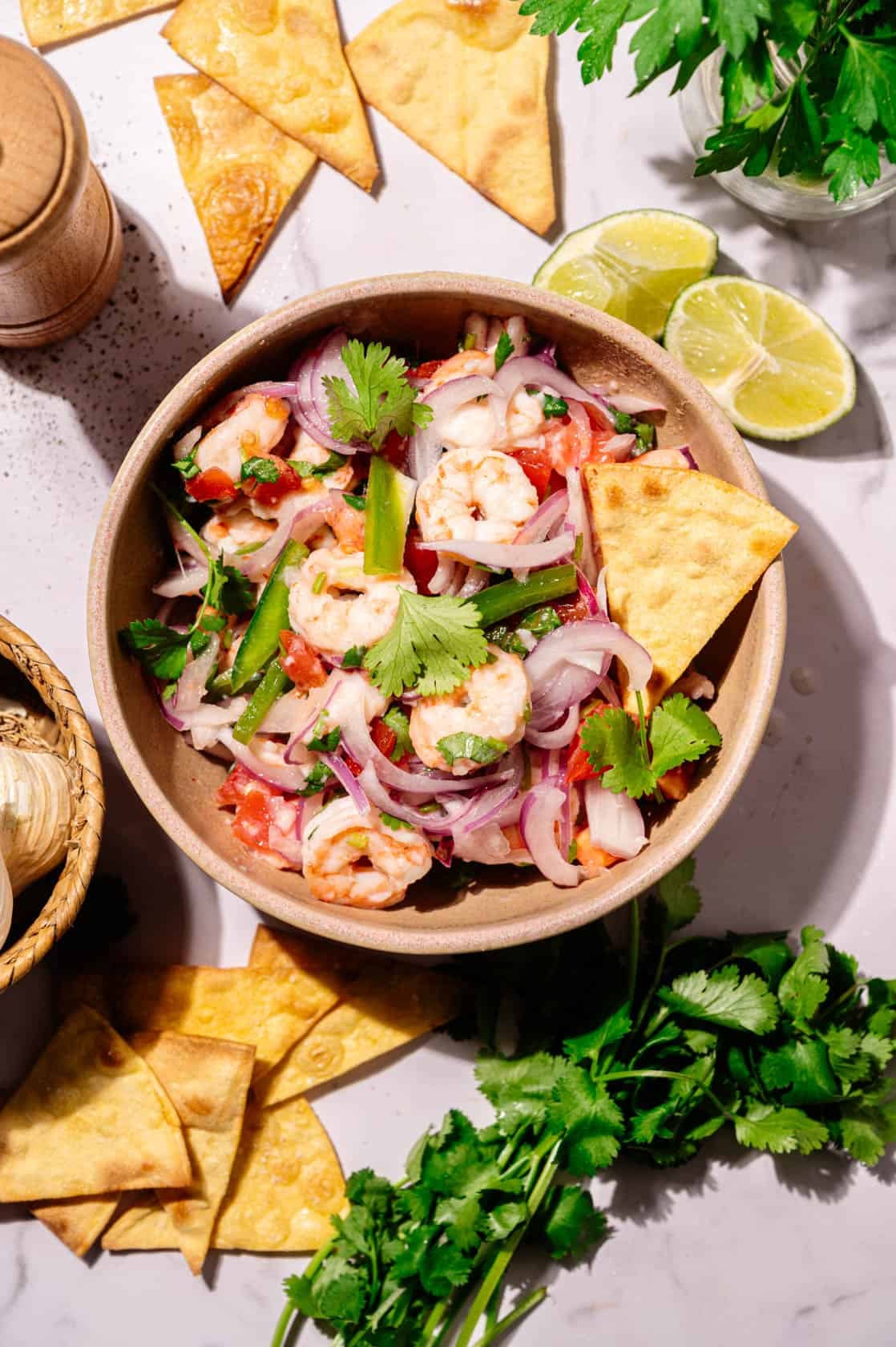 Ecuadorian shrimp ceviche with lime, cilantro, red onion and tortilla chips on a marble surface.