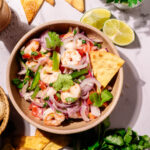 Shrimp ceviche in a rustic bowl served with crispy tortilla chips, lime wedges and fresh cilantro.