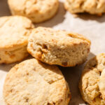 A close-up of golden, flaky almond biscuits stacked and overlapping on a parchment-lined baking sheet.