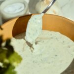 Bowl of garlic cilantro cream sauce with spoonful of thick, creamy dip lifted above the bowl for tacos and bowls