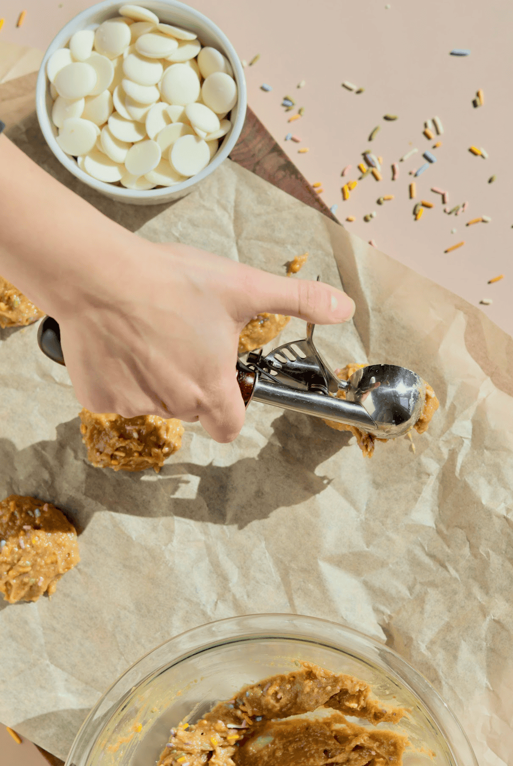 A glass bowl contains brown sugar pressed to one side, white liquid (likely milk or cream), and a splash of vanilla extract—perfect beginnings for no-bake dessert favorites like birthday cake truffles. Sprinkles decorate the surrounding surface.