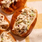 Chicken salad sandwiches on soft buns, filled with a creamy mixture of chicken, celery, and red onion, are arranged on a yellow-and-white checkered cloth.