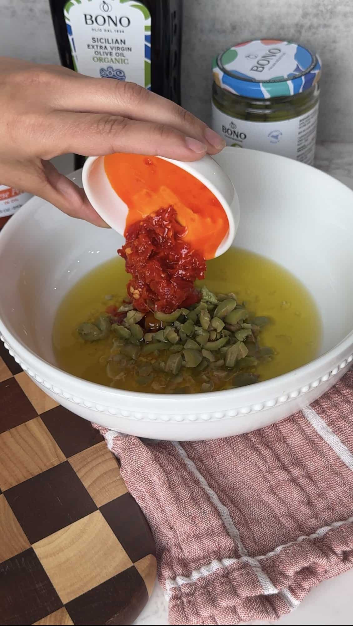 Pouring hot Calabrese pepper into a white bowl with Castelvetrano olives and Bono extra virgin olive oil to make Italian dipping oil