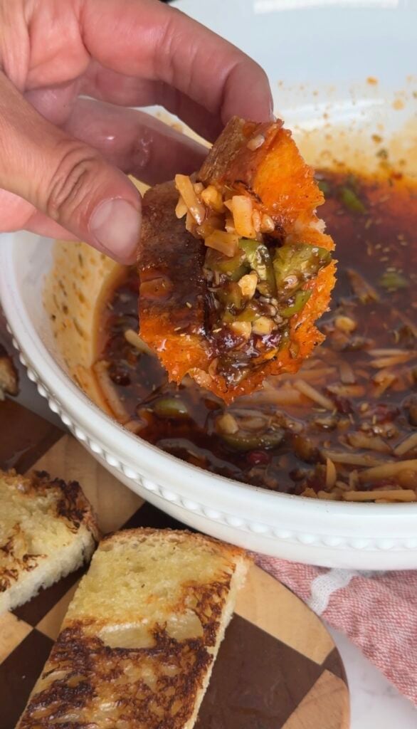 Close up shot of Hand holding a piece of toasted bread loaded with Italian herb dipping oil, olives, and balsamic