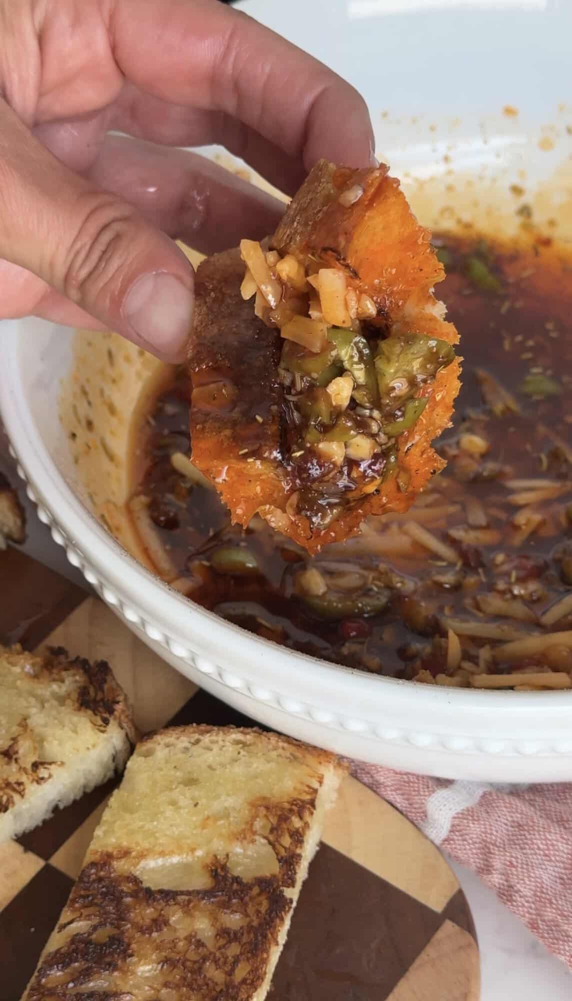 Close up shot of Hand holding a piece of toasted bread loaded with Italian herb dipping oil, olives, and balsamic