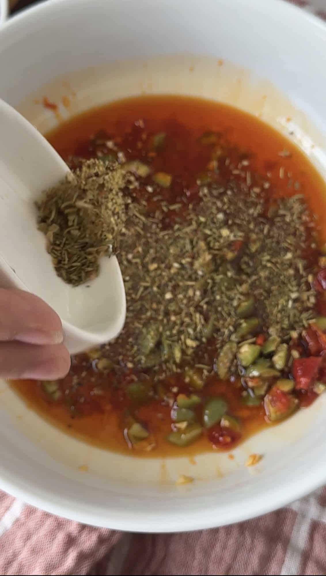 Pouring Bragg's 24 herb and spice seasoning into Italian bread dipping oil