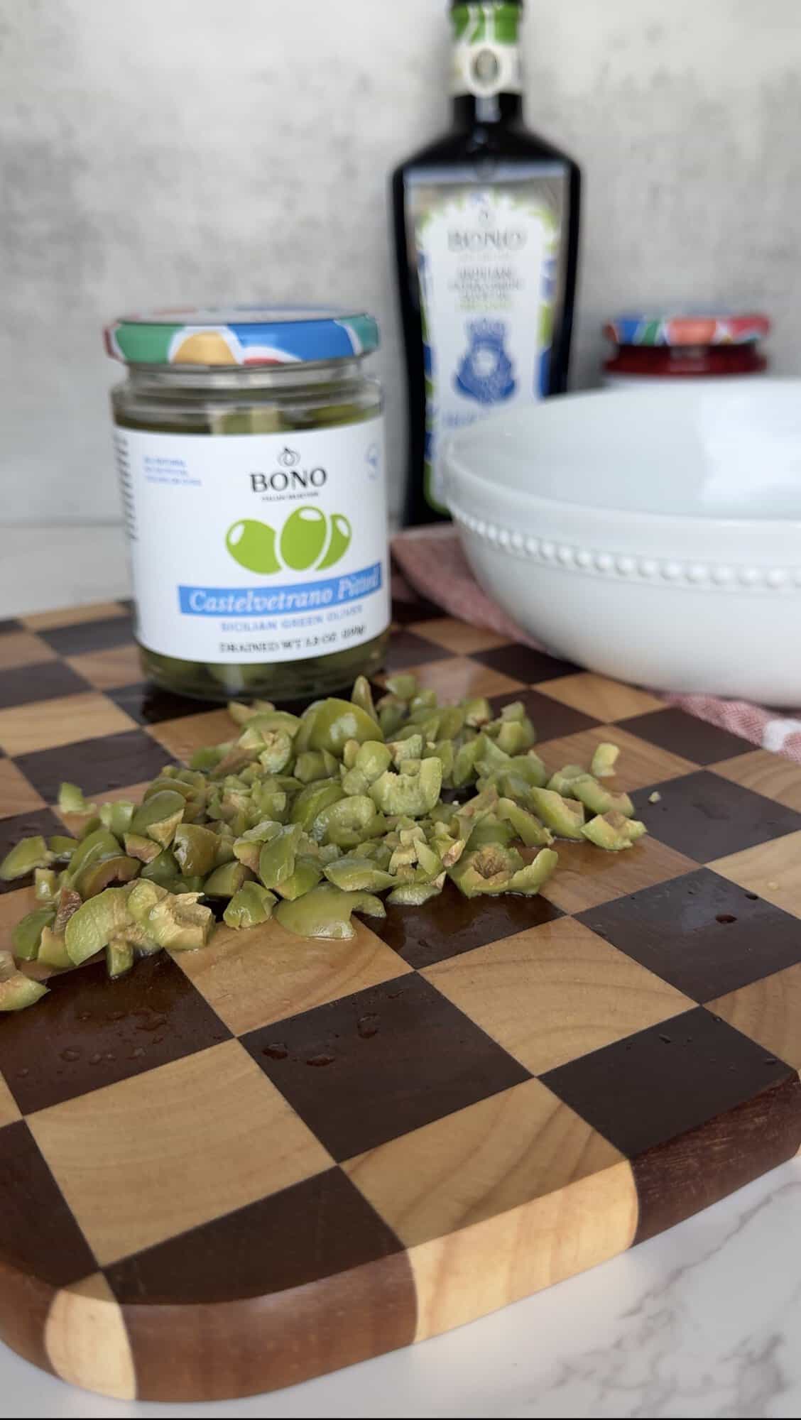 Roughly chopped Bono Castelvetrano pitted green olives on a checkered wood cutting board for Italian bread dipping oil