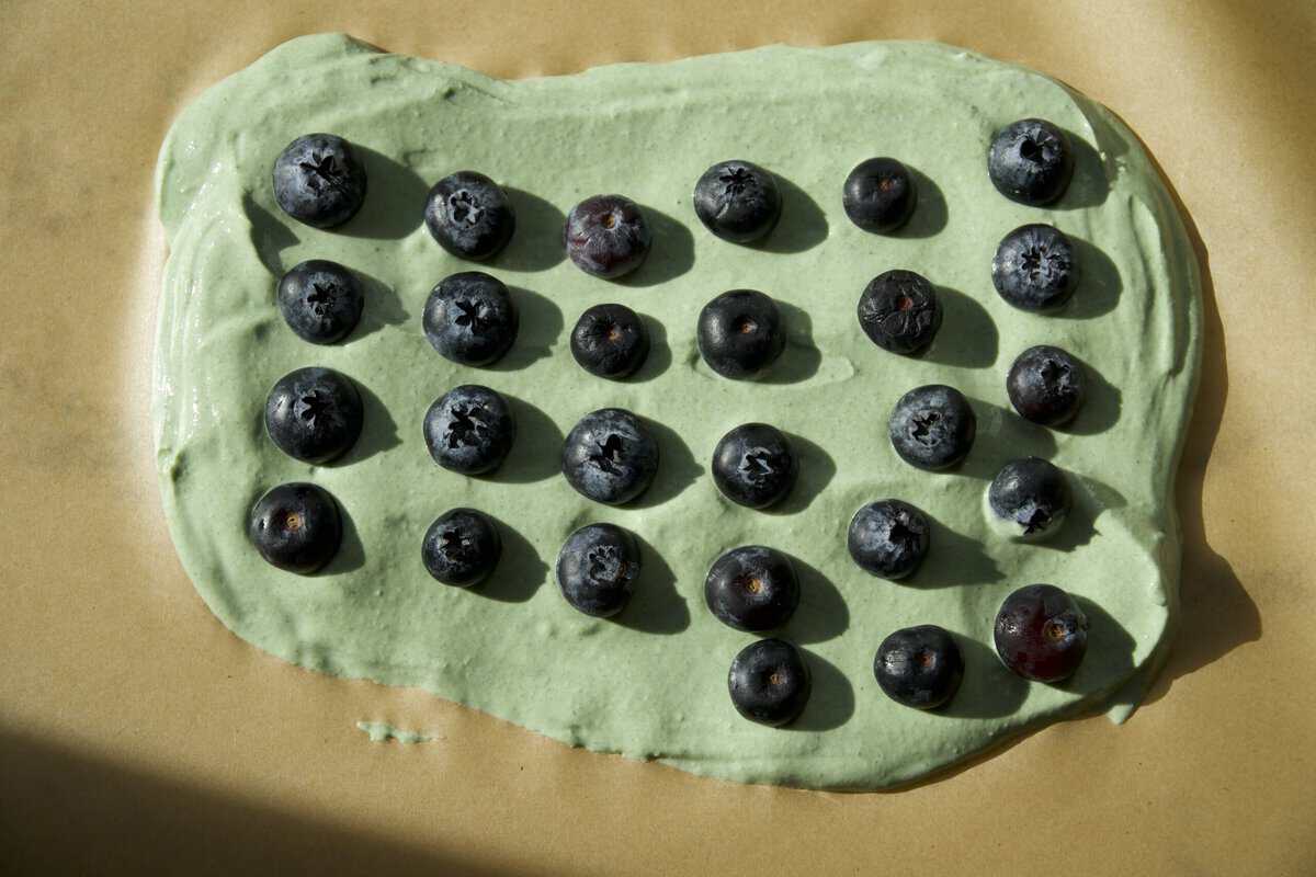 Fresh blueberries arranged in rows on green Greek yogurt spread on parchment paper