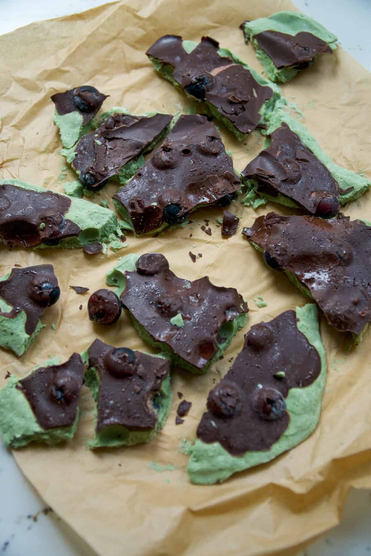 Broken pieces of frozen Greek yogurt blueberry bark with dark chocolate on parchment paper