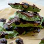 A stack of green matcha chocolate bark pieces with a dark chocolate layer and scattered whole blueberries, placed on brown parchment paper, reminiscent of the vibrant look and wholesome appeal of greek yogurt bark.