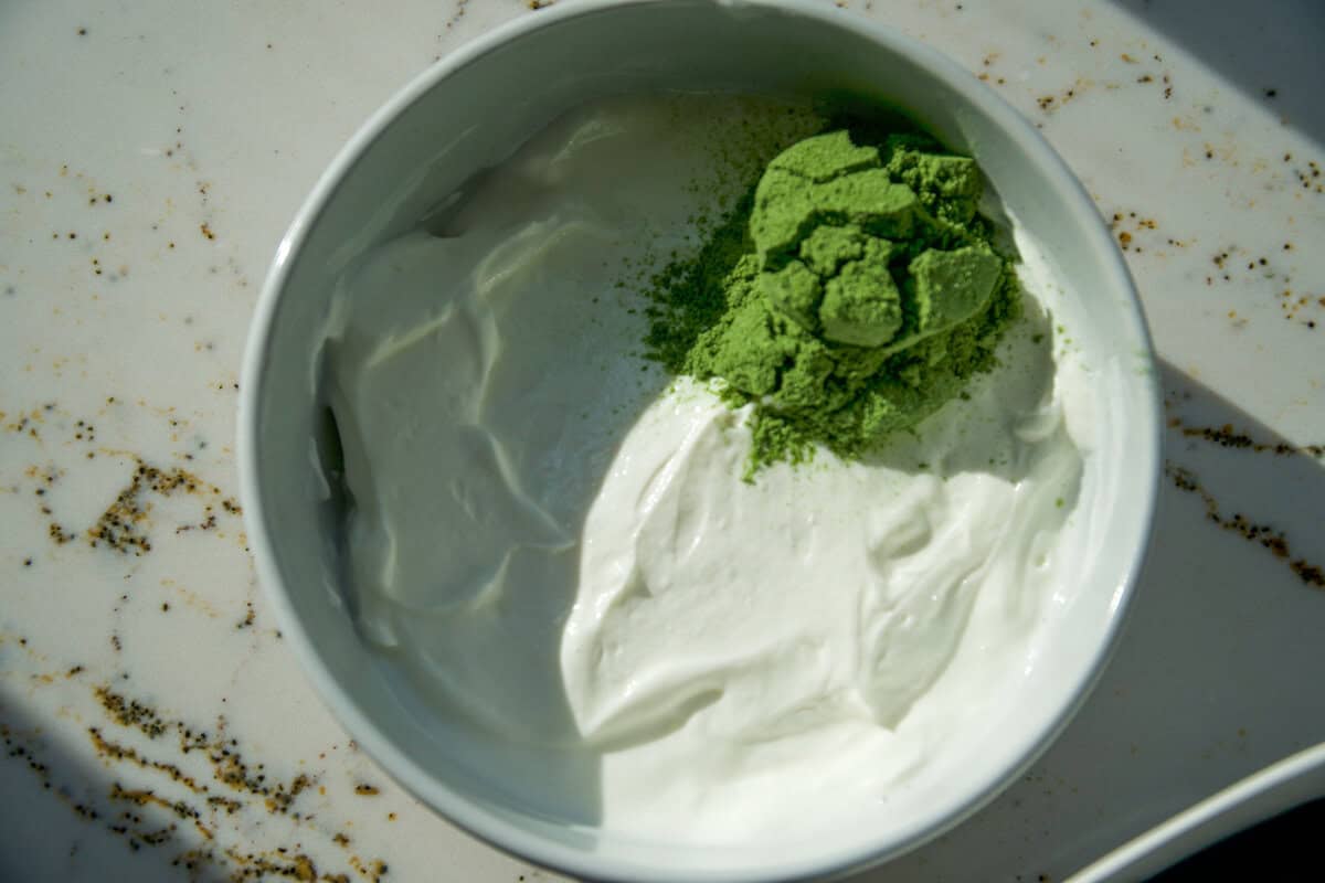 Greens powder added to plain Greek yogurt in a white bowl before mixing.