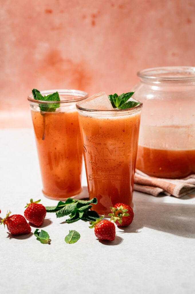 Strawberry Peach lemonades in to glass cups and a glass pitcher. Garnished with mint leaves