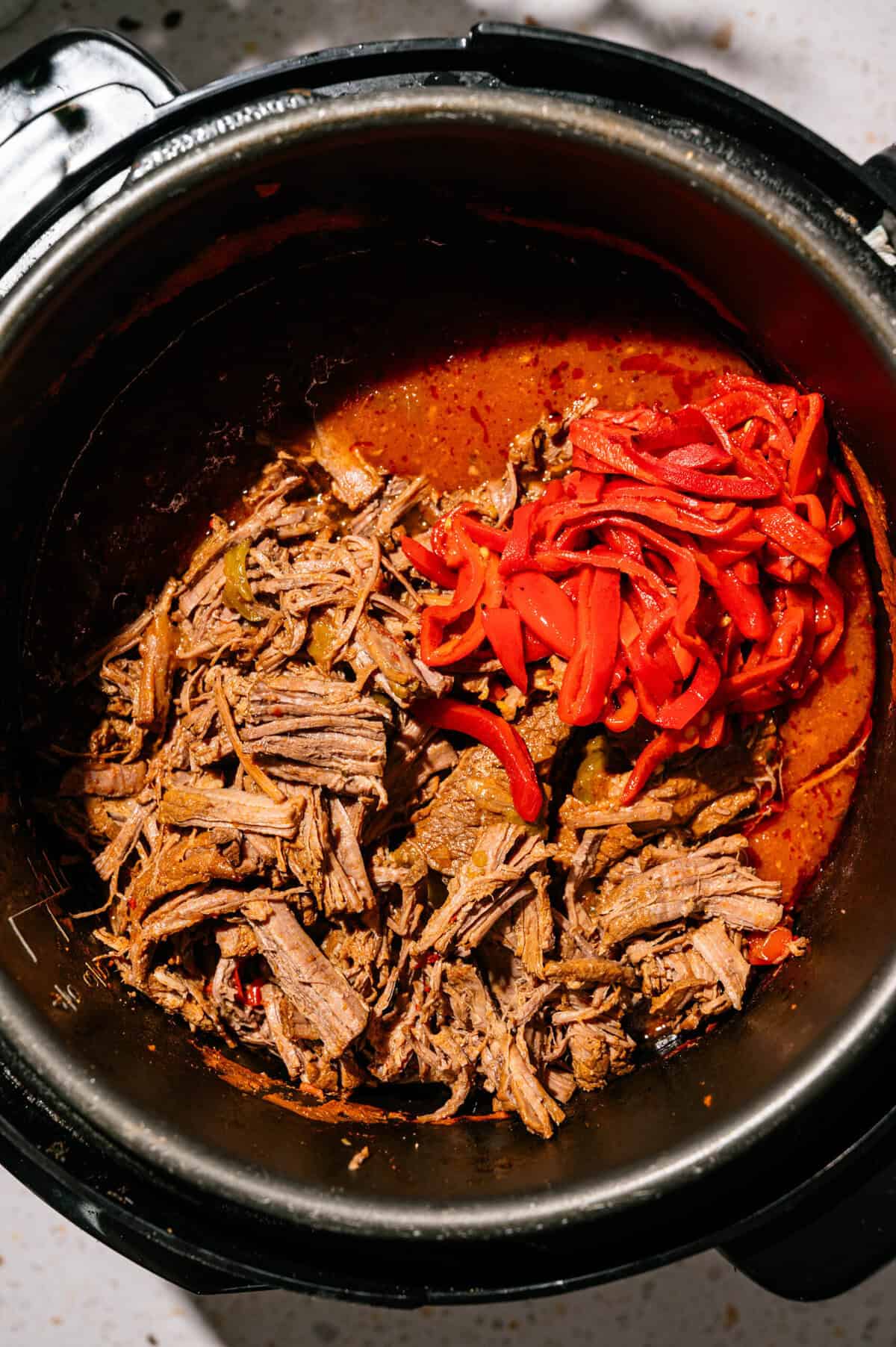 Shredded beef and sliced red bell peppers in a stew-like sauce inside a black Instant Pot, viewed from above.