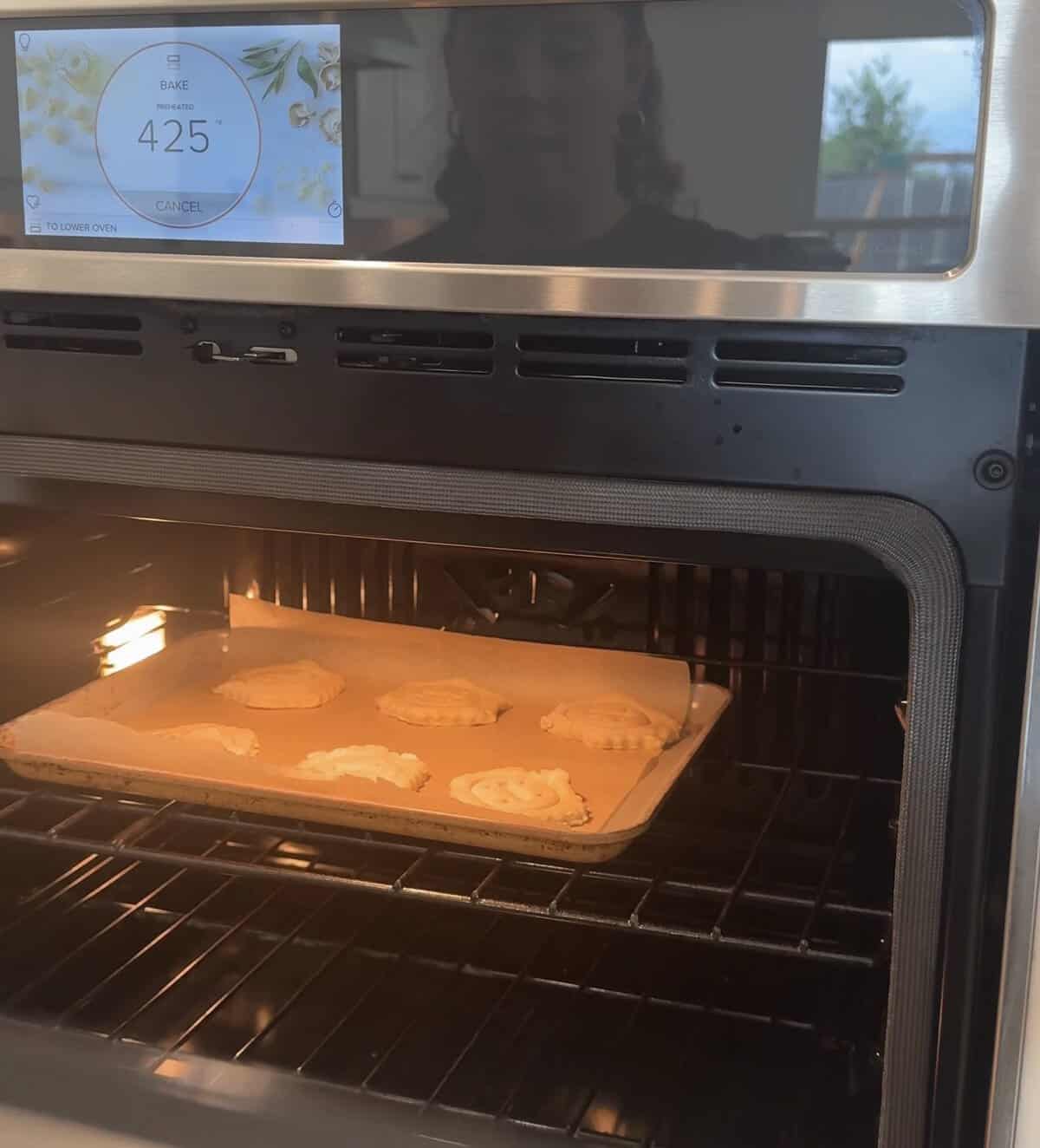 A tray of pastries is baking in an oven set to 425°F. The oven has a digital touchscreen display, and a faint reflection of a person is visible in the oven door.