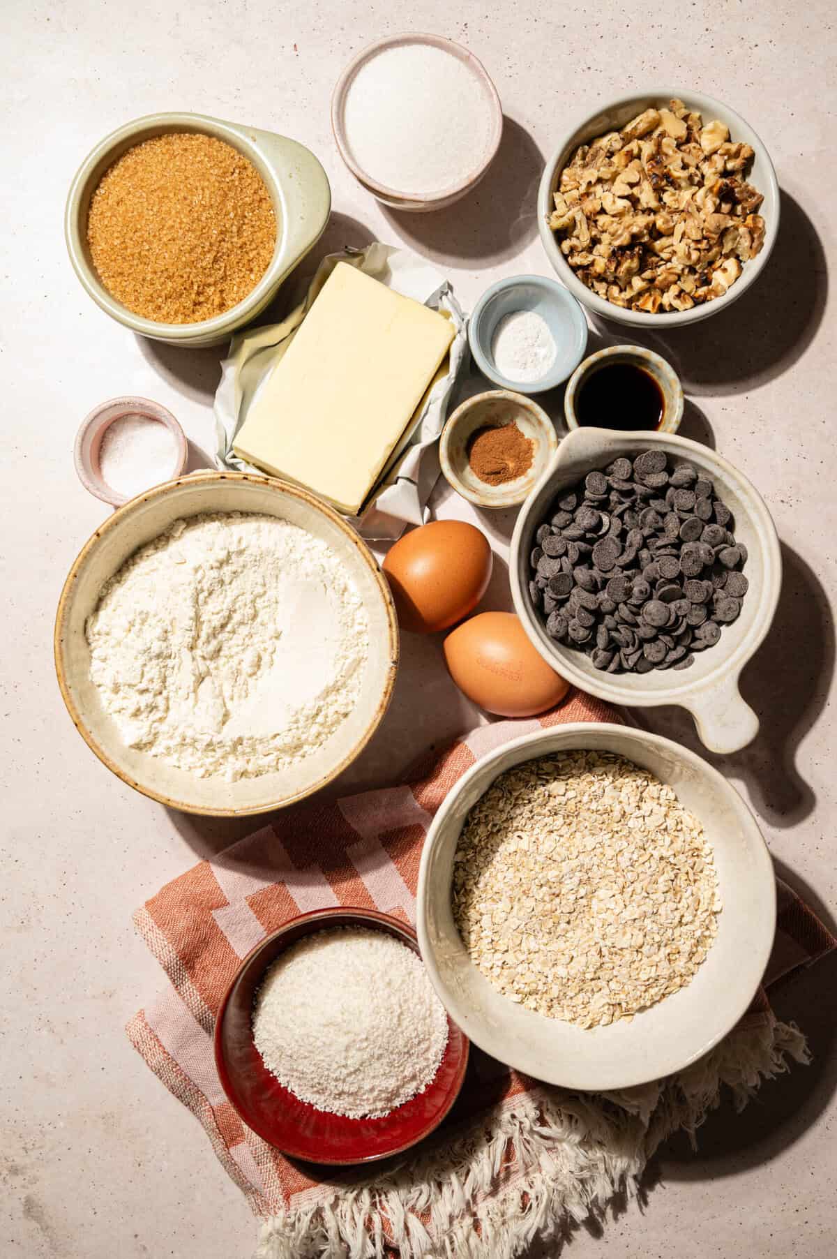 Ingredients for a brown butter oatmeal chocolate chip skillet cookie: butter, flour, oats, brown sugar, sugar, eggs, chocolate chips, coconut, walnuts, cinnamon, and vanilla