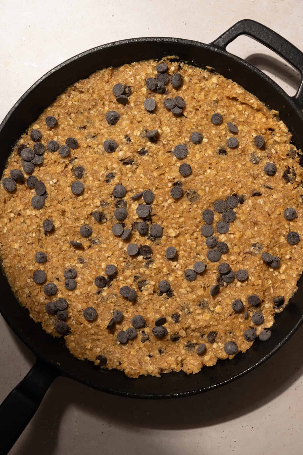 Extra chocolate chips pressed on top of oatmeal cookie dough in a cast iron skillet