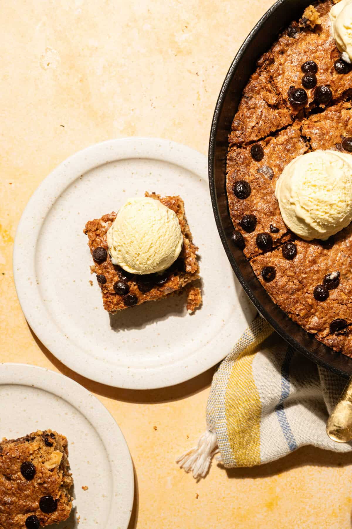 Square of brown butter skillet cookie topped with vanilla ice cream on a white plate