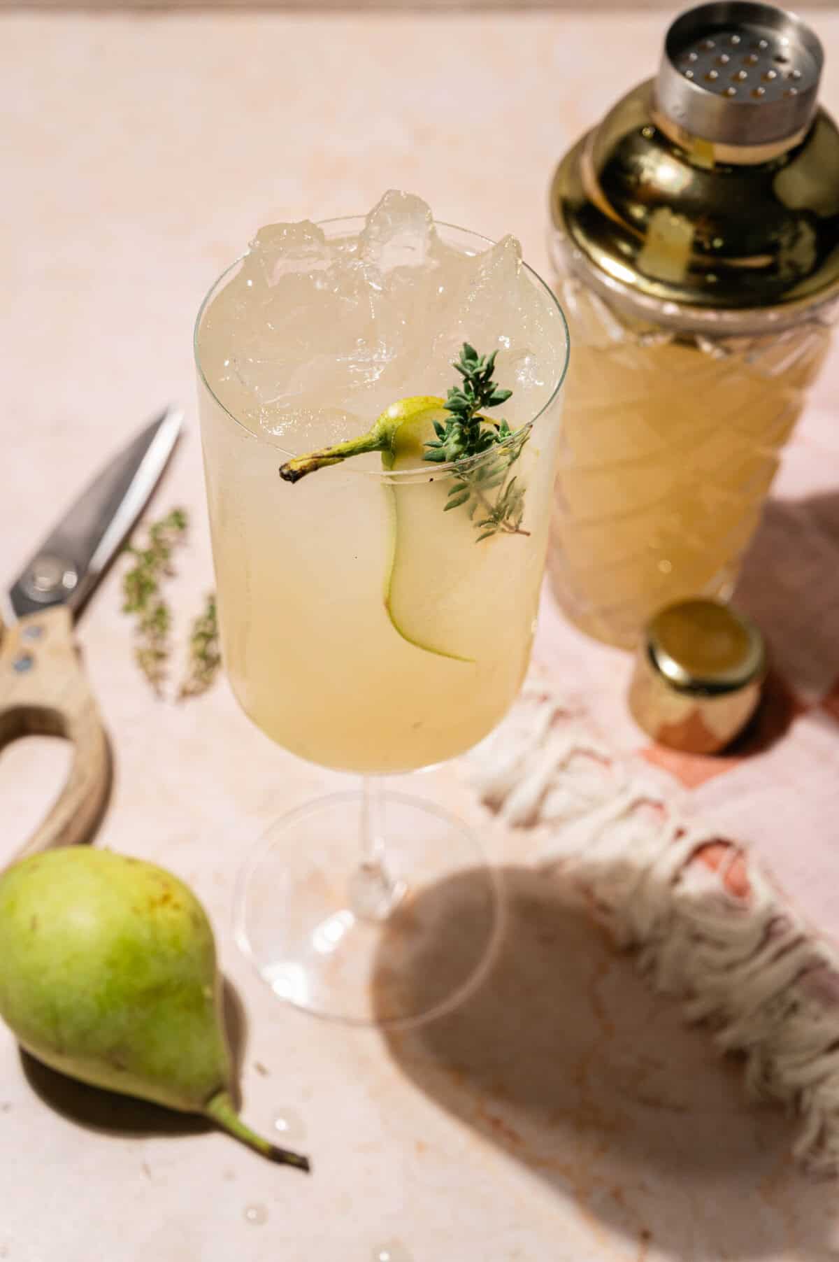 Fall vodka cocktail with pear and thyme served over ice beside a gold cocktail shaker