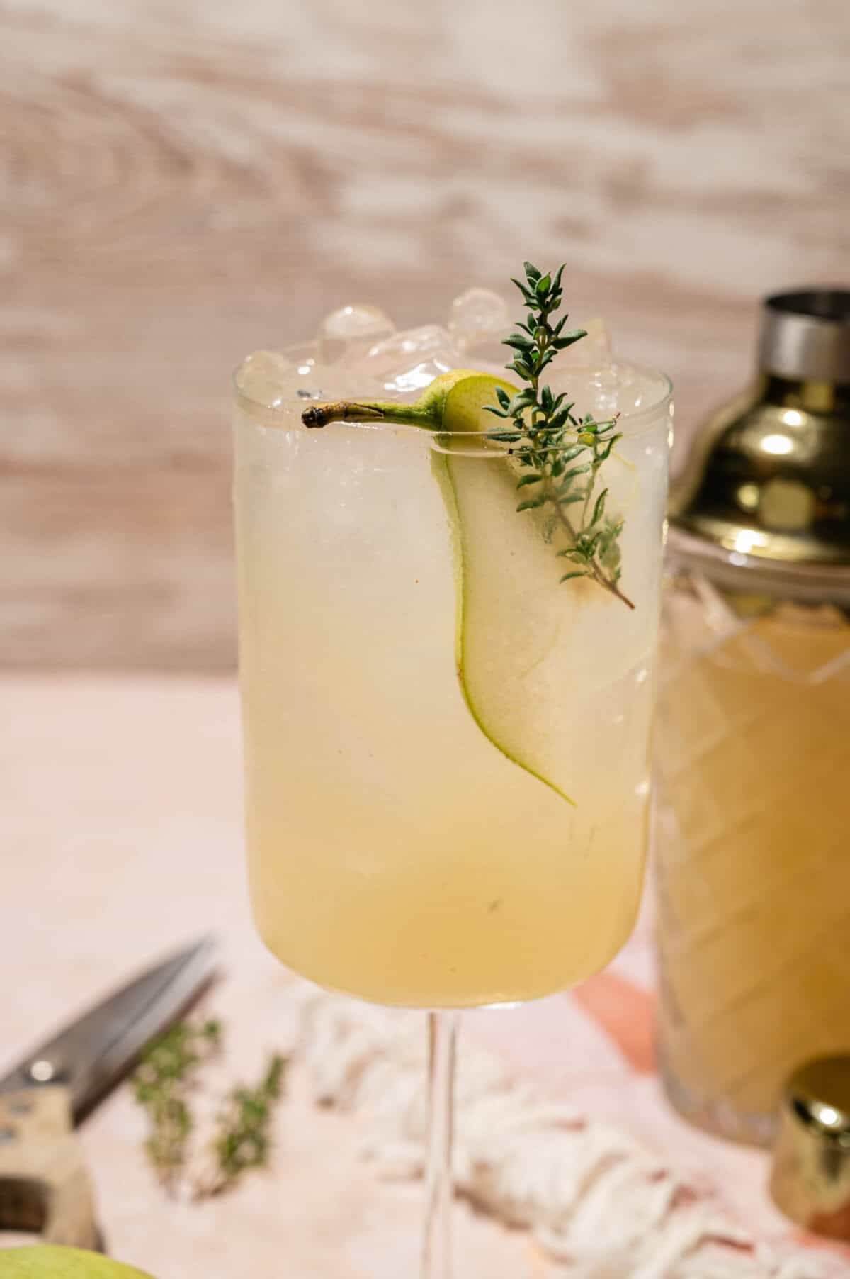 Easy pear cocktail topped with crushed ice and garnished with a pear slice and thyme sprig