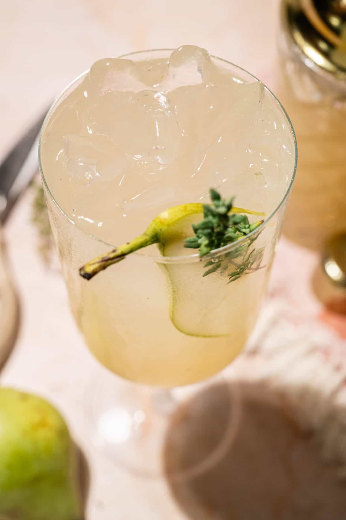 Close-up of crushed ice, a thin pear slice, and fresh thyme garnishing a pear cocktail